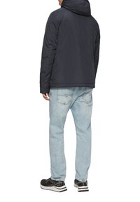 Marineblauer Kapuzenjacke mit strukturierter Oberfläche, kombiniert mit hellblauen Jeans. Die Schuhe haben ein schwarz-weißes Design, das den insgesamt lässigen Look unterstreicht.