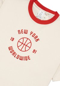 T-shirt crema a maniche corte con colletto a coste rosso e grafica ricamata. Il testo recita "NEW YORK," un pallone da basket e "WORLDWIDE 1991."