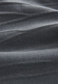 Tissu gris foncé avec un motif de tissage diagonal visible et des plis doux créant des variations subtiles de lumière et d'ombre.