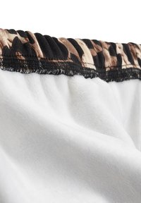 Weißer Fleece-Stoff mit einem gerafften schwarzen Gummibund, der ein Leopardenmuster in Brauntönen und Beige aufweist.