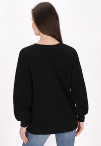 Felpa nera con maniche lunghe a sbuffo, scollatura rotonda e finitura testurizzata; indossata con jeans azzurri, vista da dietro.