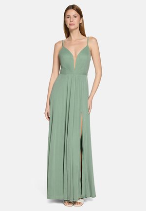 Kvinde iført en gulvlængde salviegrøn kjole med tynde stropper, dyb V-udskæring og høj slidser på venstre side, stående mod en hvid baggrund.