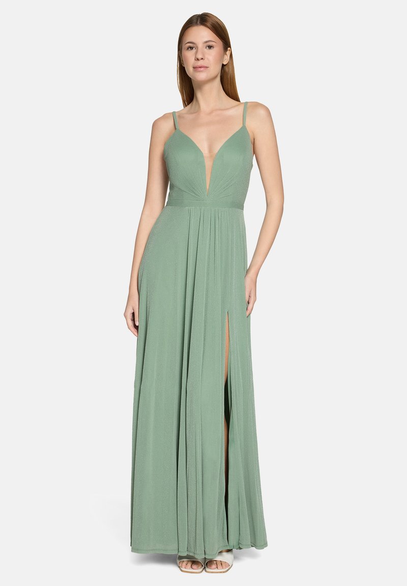Kobieta w długiej sukni koloru szałwiowego z cienkimi ramiączkami, głębokim dekoltem w kształcie litery V oraz wysokim rozcięciem po lewej stronie, stojąca na białym tle.