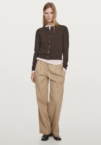 Hnědý cardigan se zlatými knoflíky přes bílou košili, doplněný béžovými širokými kalhotami. Hladká látka, minimalistický design, pohodlný střih.