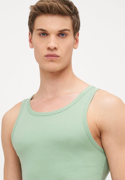 Débardeur vert clair en coton, doté de larges bretelles et d'une coupe ajustée, texture lisse avec un fin relief.