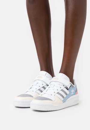 Baskets blanches avec un mélange de textile gris et des accents bleu clair. Elles présentent trois rayures grises et une sangle en Velcro. Semelle en caoutchouc texturé.