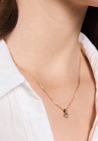 Złoty łańcuszek naszyjnik z ozdobnym wisiorkiem z turkusowym kamieniem, wyeksponowany na białej koszuli z kołnierzykiem.