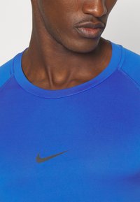 Blå performance t-shirt med rund halsudskæring og korte raglanærmer. Har et sort Nike-logo i midten. Glat tekstur.