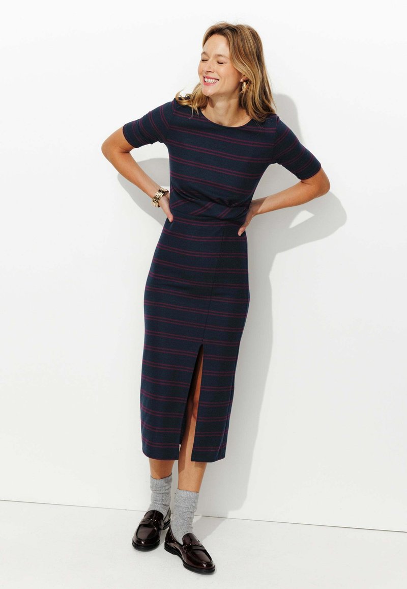 Robe rayée en marine avec des lignes bordeaux, longueur genou avec une fente sur le côté. Tissu doux, encolure ronde, forme ajustée, manches courtes.