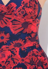 Ärmlös klänning med en figurnära bodice, mörkblått tyg med stora röda blommönster, strukturerat med svarta accenter och en utsvängd kjol.