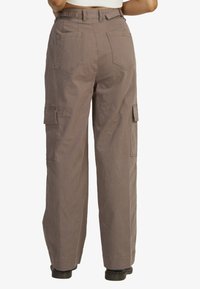 Cargo pants in taupe, featuring a high waist, wide leg, large side pockets, and stitched detailing. Made from durable cotton fabric.