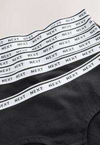 Culottes en coton noir avec plusieurs ceintures élastiques blanches, portant le nom de la marque « NEXT » en texte noir. Texture lisse, design simple.