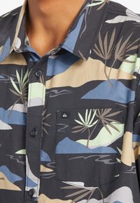 Koszula na krótki rękaw na guziki z ciemnego materiału, zdobiona wielokolorowym krajobrazem i wzorem palm, z kieszenią na piersi i detalem z logo.