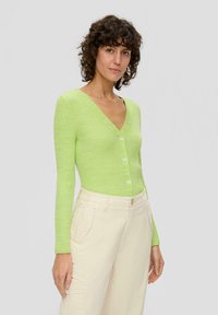 Cardigan côtelé vert clair avec un col en V, doté de quatre boutons sur le devant et de manches longues, associé à un pantalon cargo beige.