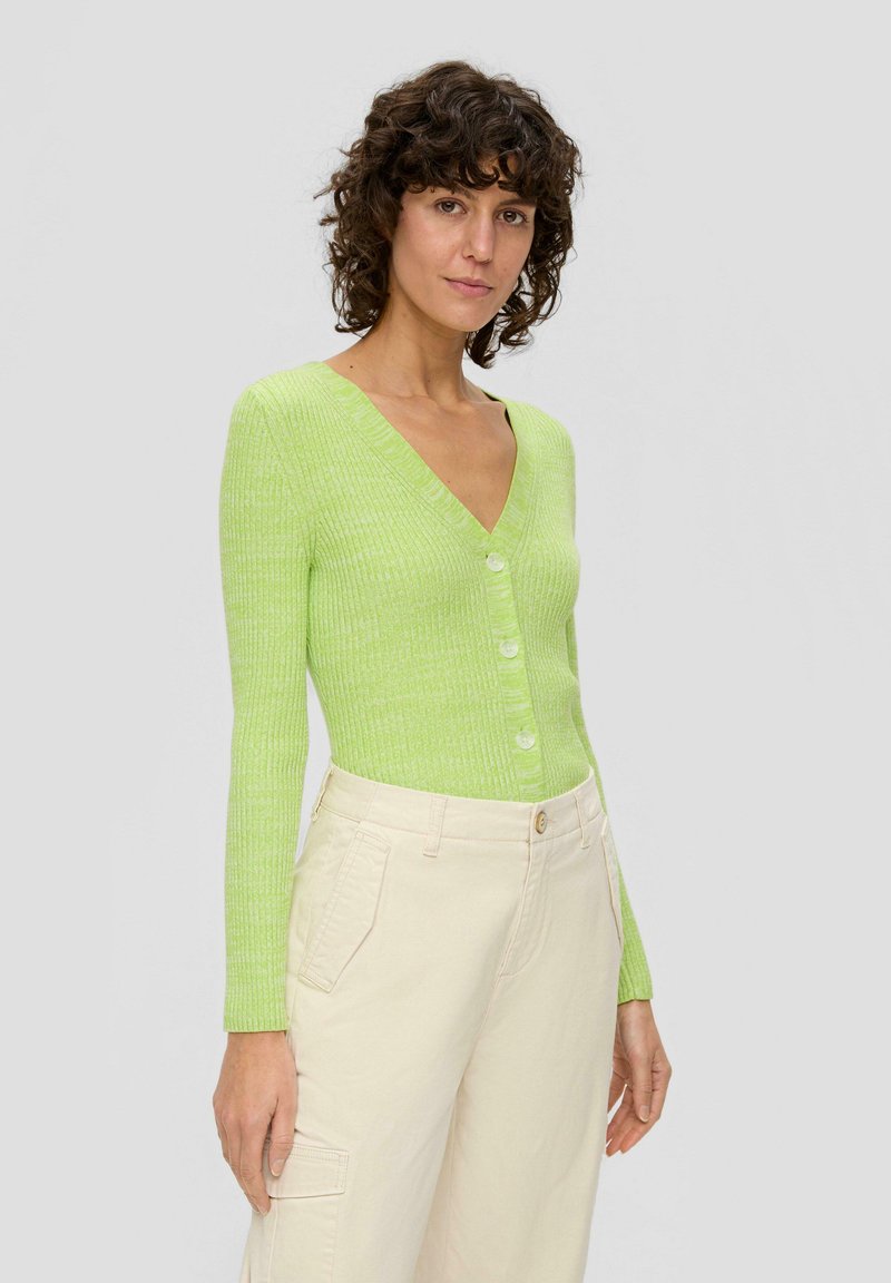 Cardigan côtelé vert clair avec un col en V, doté de quatre boutons sur le devant et de manches longues, associé à un pantalon cargo beige.