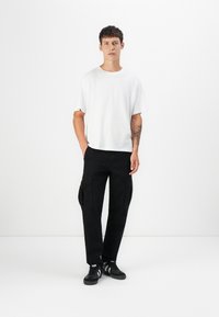 Hvid bomulds T-shirt med afslappet pasform parret med sorte cargo bukser med sidelommer, iført sorte sneakers. Ensfarvet baggrund.