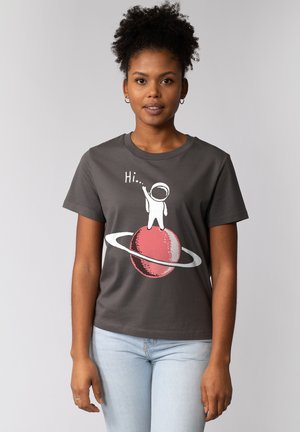 T-shirt en coton gris avec un graphique d'astronaute blanc saluant sur une planète rouge avec un anneau. Manches courtes, design col rond, coupe décontractée.