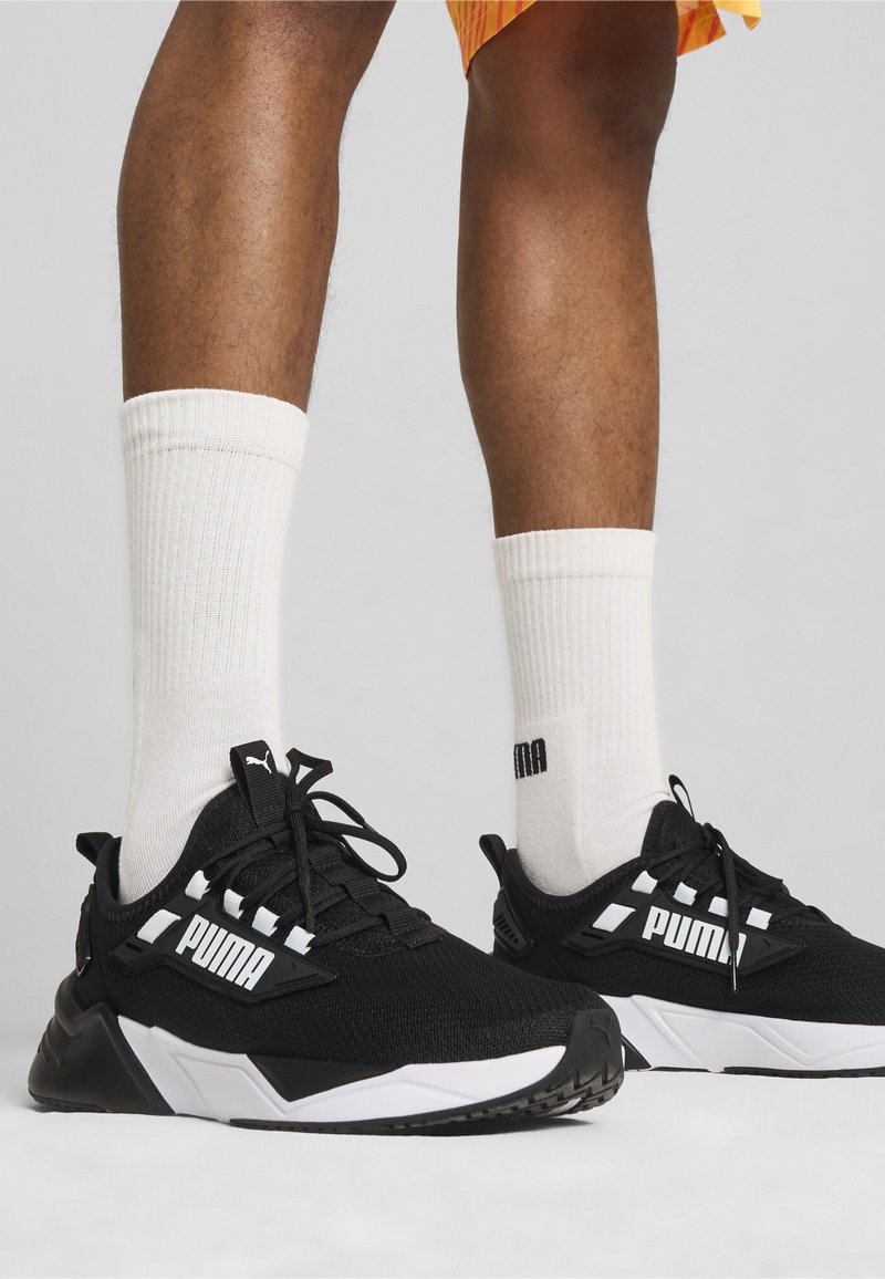 Baskets de sport noires avec une tige texturée, des accents blancs et un système de laçage. Associées à des chaussettes blanches côtelées mi-mollet.