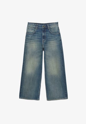 Jeans en denim bleu à jambes larges avec des patchs décolorés, conception à cinq poches, passants de ceinture et fermeture éclair. Texture usée près des poches.