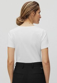 Witte katoenen T-shirt met korte mouwen en een ronde halslijn, van de achterkant getoond. Draag het met zwarte op maat gemaakte broek met achterzakken.
