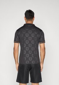 Polo cinzento escuro com um padrão subtil de escudos, acentuado por uma gola e bainha das mangas em vermelho e verde.