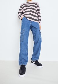 Långärmad randig skjorta i rosa och grått, kombinerad med blå cargobyxor med sidofickor och svarta sneakers med vita sulor.