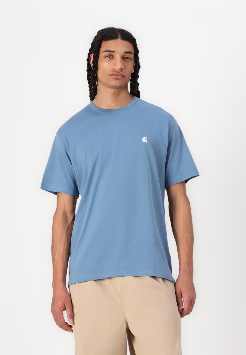 T-shirt en coton bleu clair avec des manches courtes, un col rond et un petit logo blanc sur la poitrine. Coupe légèrement décontractée.