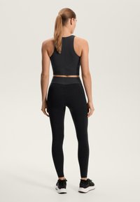 Crni set sportske odjeće koji uključuje kratki top s teksturiranim uzorkom i tajice visokog struka. Oba dijela imaju glatku završnicu i tijelu pristajajući kroj.