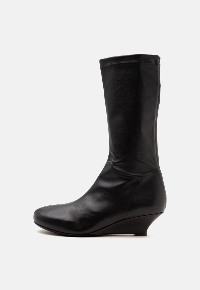 Botte en cuir noire mi-mollet avec un bout arrondi et un petit talon compensé, présentée sur un fond blanc uni.
