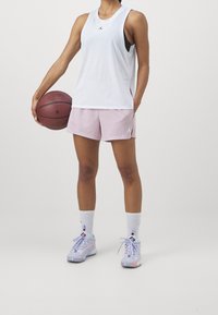 Vit ärmlös tanktop, rosa mesh shorts, vita strumpor, och mångfärgade sneakers. Håller en basketboll. Jordan-logotyp synlig.