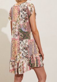 Sukienka patchworkowa z kwiatowymi i geometrycznymi wzorami w pastelowych kolorach, takich jak różowy, zielony i biały, z falbaną u dołu i krótkimi rękawami.