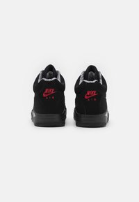 Černé tenisky Nike Air ze semišového materiálu, s červenými akcenty loga a vzorovaným černobílým límcem. Pevná černá podrážka.