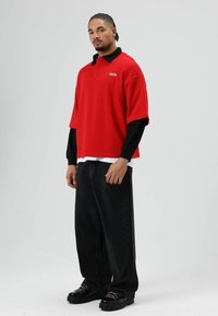 Rode oversized poloshirt met een zwarte kraag, gedragen over een wit shirt, gecombineerd met losse zwarte jeans en zwarte laarzen met roze veters.