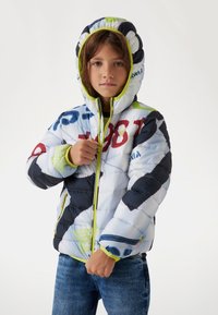 La giacca imbottita presenta una base blu chiaro con accenti blu scuro e verdi, stampe grafiche, un colletto alto e una chiusura a zip.
