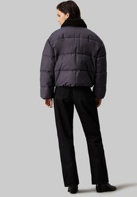 Zwarte gewatteerde jas met een korte, boxy silhoutte en een zwarte nep bont kraag. Gedirigeerd met hoge taille zwarte broeken en enkellaarsjes.