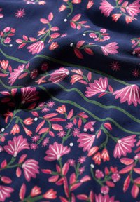 Marinefarbener Stoff mit floralem Muster; rosa Blumen, grüne Ranken und weiße Punkte. Glatte Textur mit lebendigen Farben und aufwendigem Design.