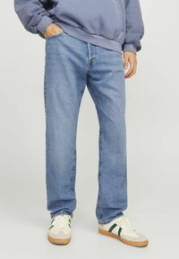 Hellblaue Jeans mit geradem Bein, ausgestattet mit fünf Taschen und einer leichten Ausbleichung. Kombiniert mit cremefarbenen Sneakers und einem grauen Hoodie.