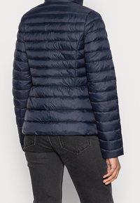Giacca puffer blu marina con motivo a righe orizzontali, colletto alto e design aderente. Tessuto liscio, isolamento caldo, abbinata a jeans scuri.
