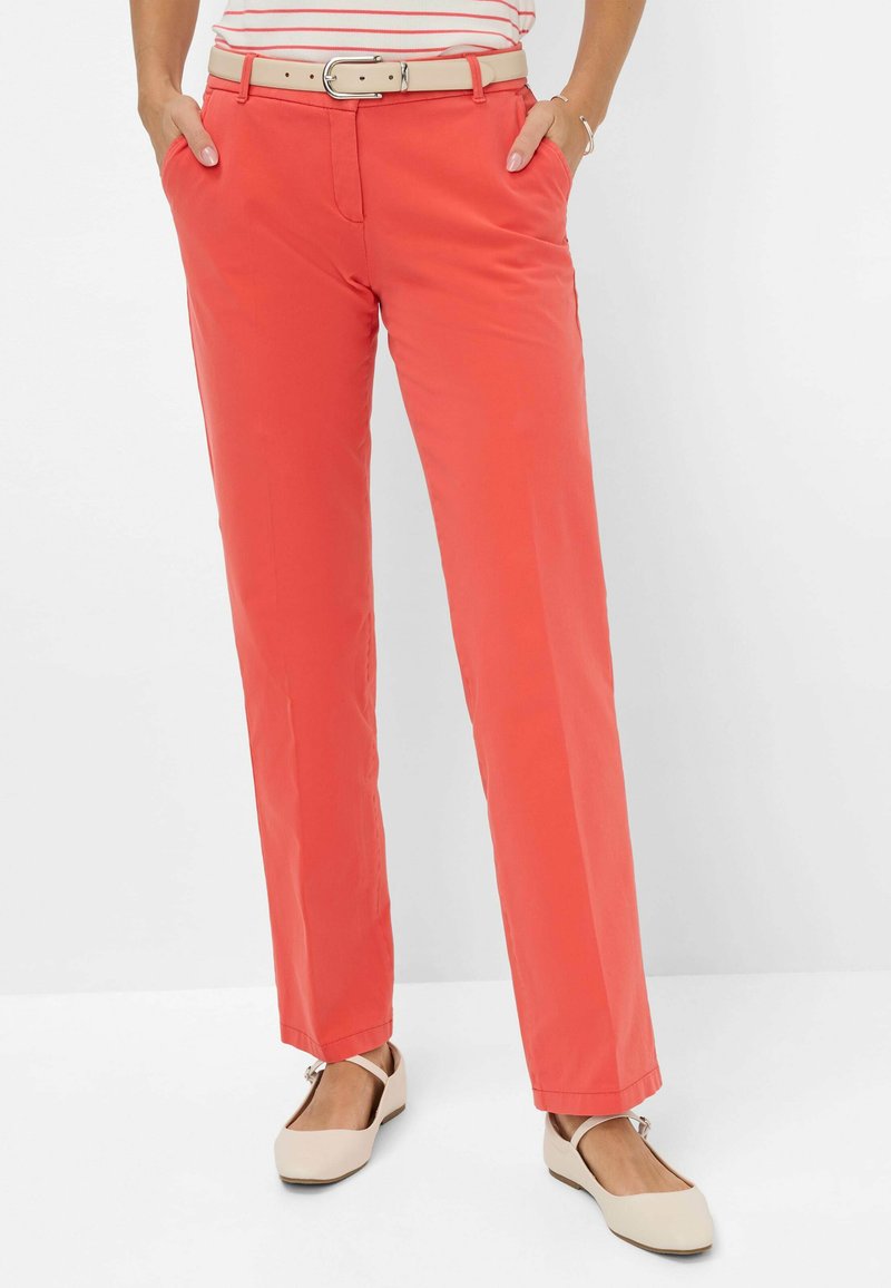 Koraalkleurige broek met een rechte pasvorm, voorzien van zijzakken en een riem. Het materiaal lijkt glad en lichtgewicht. Gestyleerd met beige flats.