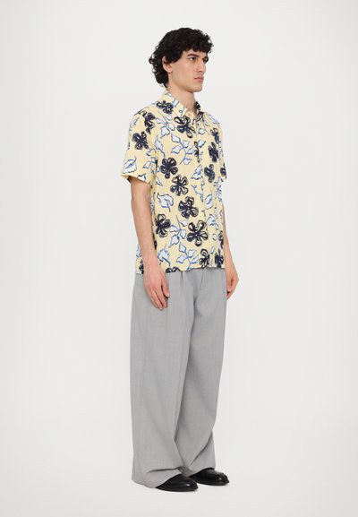 Short-sleeve floral shirt with a yellow background, black and blue flower motifs, paired with light gray wide-leg trousers and black shoes.