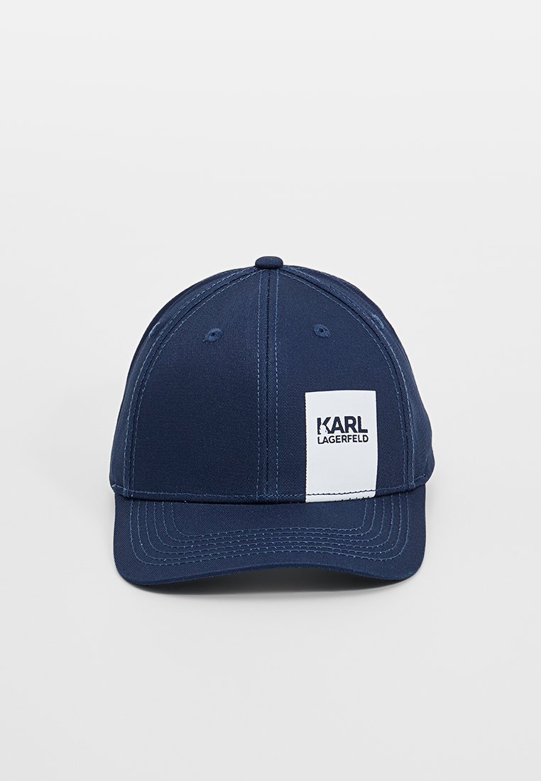 Casquette de baseball bleu marine avec un design structuré, présentant une patch logo blanc rectangulaire et des coutures contrastantes sur la visière.