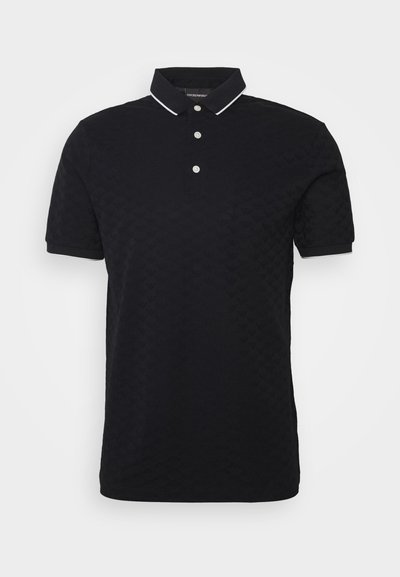 Temno modra polo majica iz teksturiranega bombaža s kragnico, tremi gumbi in belimi poudarki na kragnici in rokavih.