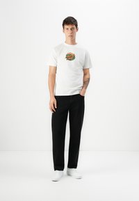Witte katoenen T-shirt met een kleurrijke grafische print op de borst, gecombineerd met zwarte broek en witte sneakers. Eenvoudig, casual ontwerp.