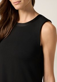 Haut sans manches noir avec une texture lisse, un col rond et des finitions en satin avec des accents de boutons visibles sur l'épaule.
