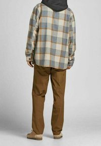 Camicia di flanella a quadri nei toni crema, blu e marrone; vestibilità rilassata con cappuccio nascosto. Abbinata a pantaloni marroni e scarpe beige.