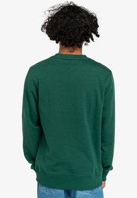 Felpa verde a girocollo con una texture morbida e polsini a coste. Presenta un design semplice, senza loghi o motivi visibili.