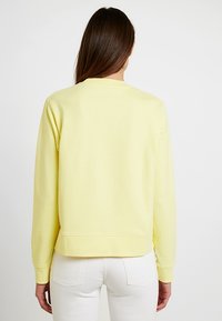 Sudadera amarilla con cuello redondo, mangas largas y diseño recortado. Confeccionada en tejido suave, con puños y dobladillo acanalados.