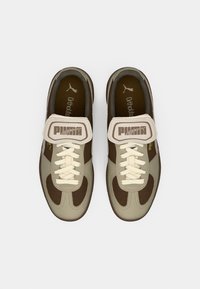 Kerged jalatsid, mille ülaosa on helesinine, tumeda pruuni aktsendiga, kreemilised paelad ja velcro rihm, millel on "PUMA" logo. Näha on Ortholite sisetald.