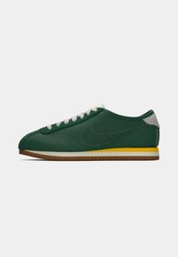 Basket low-top en cuir vert avec lacets blancs, logo perforé sur le côté, semelle intermédiaire jaune et blanche, et semelle extérieure striée marron.