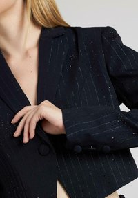 Blazer corto navy a righe verticali, tessuto testurizzato, dettagli in paillettes, chiusura a doppi bottoni e rever a punta.
